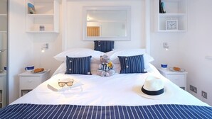 Une chambre d’hôtel bien aménagée, avec un grand lit, une table de chevet, une commode, un miroir et une étagère sur laquelle sont posés une horloge et des objets décoratifs.