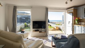 Un salon moderne doté d’un grand téléviseur, de sièges confortables, d’une vue sur la mer et d’un balcon aménagé avec du mobilier d’extérieur.