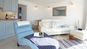 Un salon moderne comprenant un canapé, un fauteuil, une table basse et un coin cuisine avec des placards et un plan de travail.