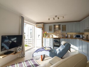 A modern living room with a flat-screen TV, a sofa, and a dining area with light blue cabinets and a kitchen in the background.