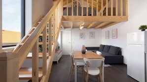 Een modern interieur met een houten trap, een eethoek met een tafel en stoelen, een bank en een koelkast.