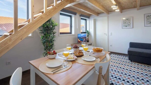 Een eetruimte met een houten tafel gedekt voor het ontbijt, een trap en uitzicht naar buiten.