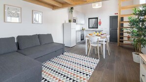 Een moderne woonkamer met een grijze bank, een kamerkleed met een patroon en een keuken op de achtergrond.