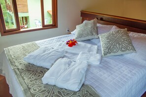 A neatly made bed with white linens, decorative pillows, and a floral arrangement. - Green Chales (Palmeiras)