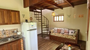 A compact kitchen with a refrigerator, wooden cabinets, a sink, and a dining area with a table and chairs. - Green Chales (Palmeiras)