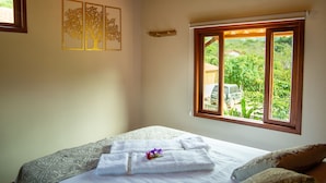 A bedroom with a bed, a window with a view of greenery, and wall art. - Green Chales (Palmeiras)