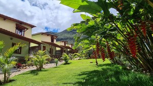 A row of two-story buildings with a green lawn and tropical plants. - Green Chales (Palmeiras)