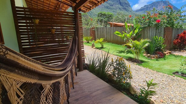 A hammock on a wooden deck, a wooden fence, and a garden with various plants and flowers. - Green Chales (Palmeiras)