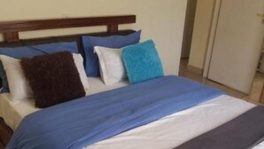 A bed with a wooden headboard, white and blue bedding, and several pillows. - Stay.Plus Blue Bells Apartment Syokimau (Mlolongo)
