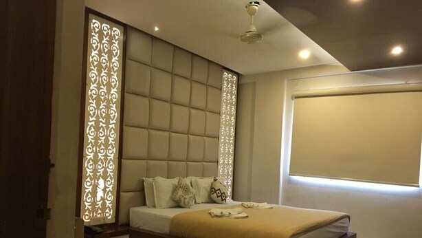 A modern bedroom with a tufted headboard, a bedside table, and a large window providing natural light. - Hotel Empark (Bengaluru)