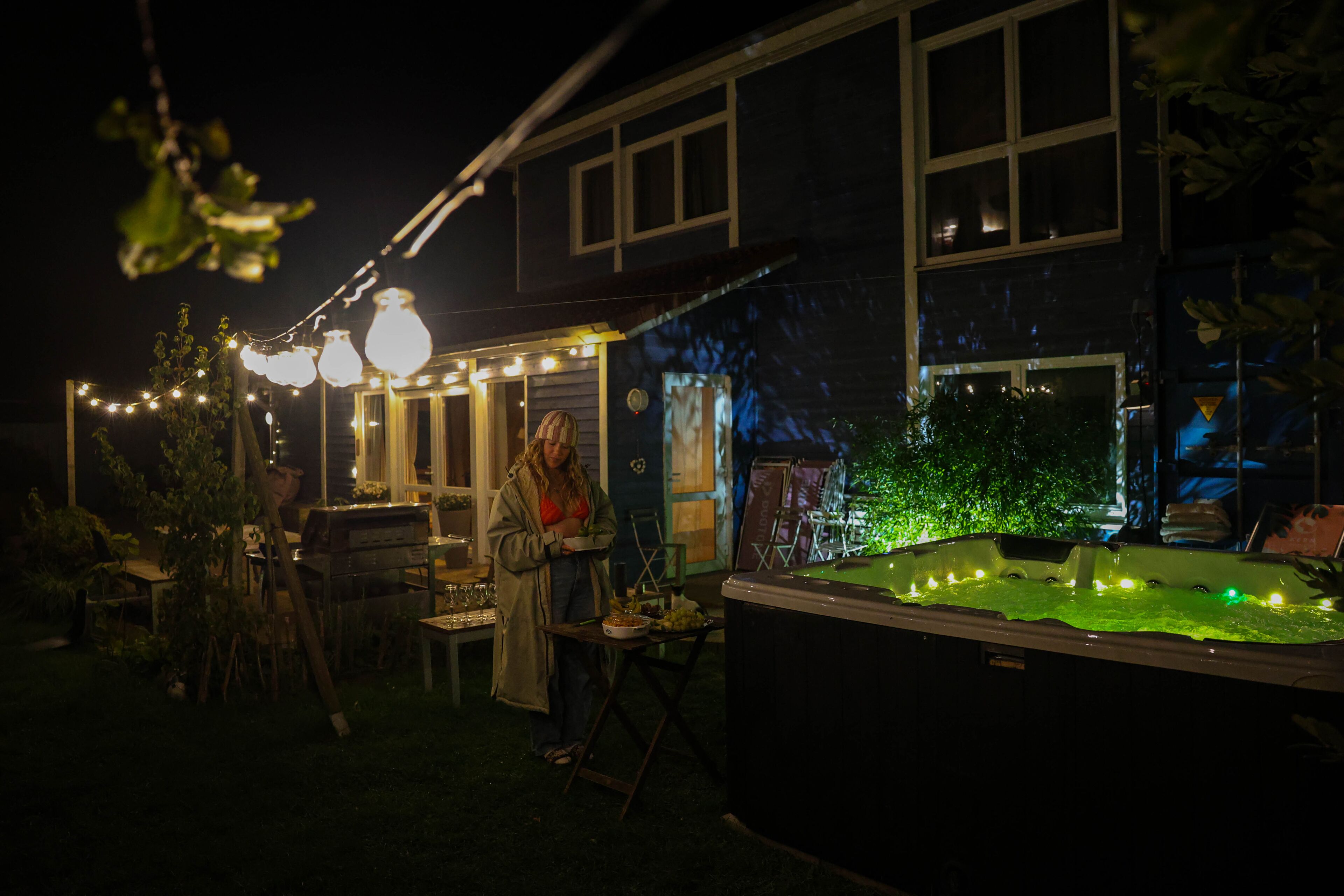 An outdoor patio area with string lights, a hot tub, and a dining table set up for an evening event.