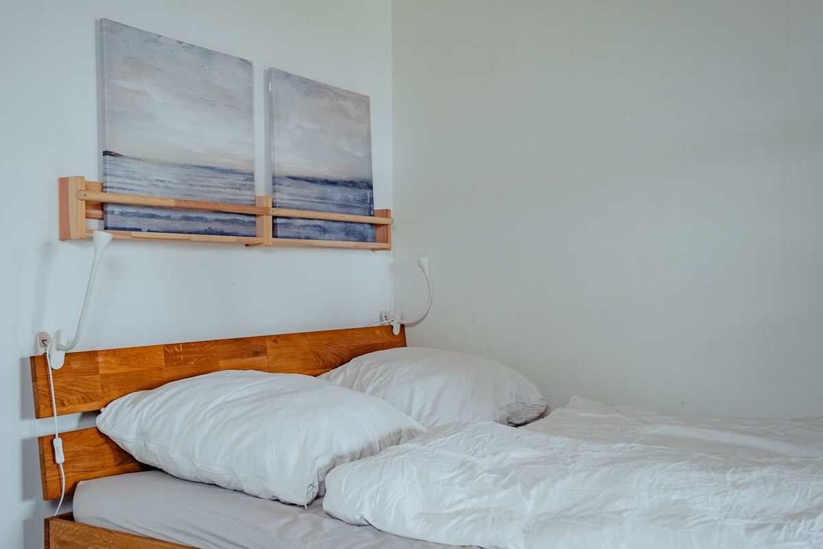 A bedroom with a wooden headboard, white bedding, and two paintings on the wall.
