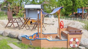 Une structure de jeu en bois, conçue comme un navire, avec une bouée de sauvetage, un petit abri et une table avec des chaises.