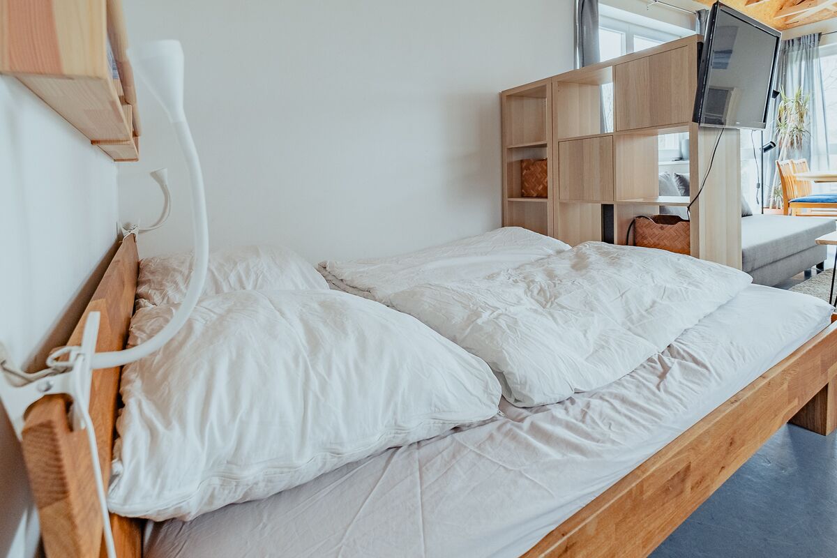 Een enkel bed met witte lakens in een kamer met een houten hoofdbord en een ingebouwde tv-plank.