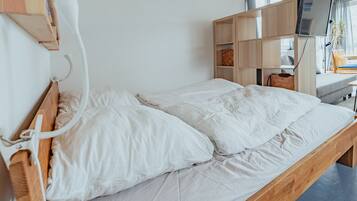 Een enkel bed met witte lakens in een kamer met een houten hoofdbord en een ingebouwde tv-plank.