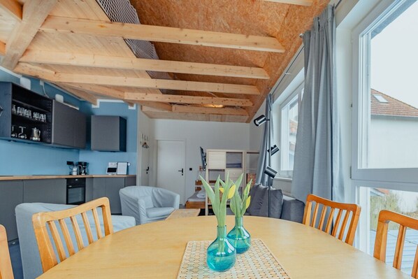 Eine moderne Küche mit Holzbalken, einem Essbereich mit rundem Tisch und Blick ins Freie.