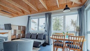 Un salon moderne comprenant un canapé, une table à manger et des chaises, de grandes fenêtres avec des rideaux et un plafond en bois.