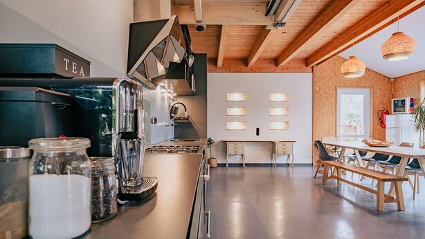 A modern kitchen with a coffee machine, jars of ingredients, and a dining area with a table and benches.