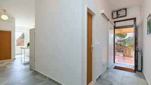 A hallway with a wooden door, a white wall, and a tiled floor.