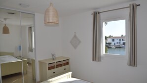 Une chambre à coucher comprenant un lit, une commode, un miroir, un luminaire suspendu et une fenêtre avec des rideaux.
