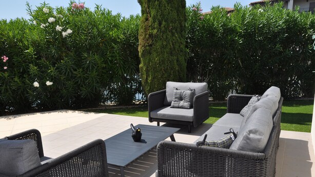 Un espace extérieur aménagé en terrasse, avec des meubles en osier, notamment un canapé et des fauteuils, ainsi qu’une petite table.