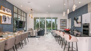 A modern kitchen with a central island, built-in oven, and a dining area with a long table and chairs.