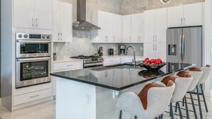 A modern kitchen with white cabinets, stainless steel appliances, and a central island with bar stools.