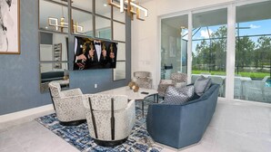 A modern living room with a large flat-screen TV, multiple seating options, and a glass door leading to an outdoor area.