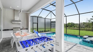 A modern indoor pool area with a foosball table, a barbecue setup, and a view of the outdoors. - Premium Home w/ Hero Theme BR, Secret Gaming RM, Theater & Pool - Near Disney (Davenport)