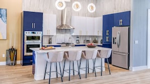 A modern kitchen with a central island, stainless steel appliances, and a blue and white color scheme. - Premium Home w/ Hero Theme BR, Secret Gaming RM, Theater & Pool - Near Disney (Davenport)