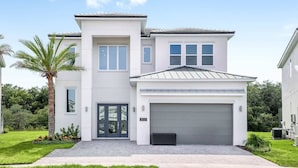 A modern two-story house with a garage, a well-maintained lawn, and a palm tree. - Premium Home w/ Hero Theme BR, Secret Gaming RM, Theater & Pool - Near Disney (Davenport)