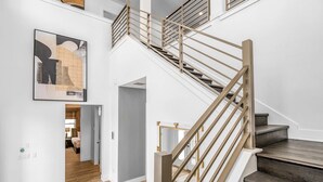 Un intérieur moderne avec un escalier en bois, une grande peinture abstraite et une vue sur une pièce comprenant un lit et une table de chevet.