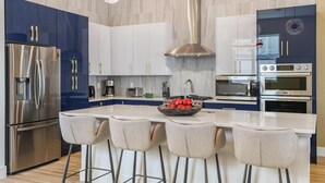 Une cuisine moderne dotée d’appareils électroménagers en acier inoxydable, d’un îlot central avec des tabourets et d’un éclairage suspendu.