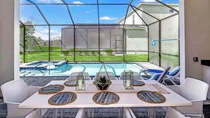 Une terrasse ensoleillée avec une piscine, des meubles en osier blancs et une véranda en verre.