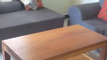Una mesa de centro de madera en una sala de estar con un sofá y una cortina estampada.