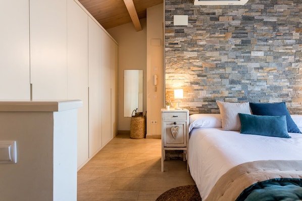 A bedroom with a stone wall, a bed with white and blue pillows, a nightstand, and a mirror.