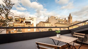 Eine Dachterrasse mit Holztisch und -stühlen, einem Blumentopf und Blick auf die Stadt.