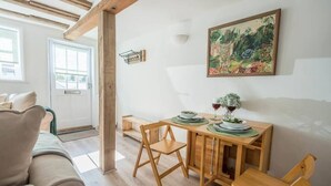A cozy dining area with a wooden table set for two, a painting on the wall, and a door leading outside. - Candy Cottage, Halesworth (Halesworth)