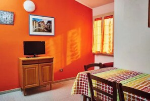 A room with a wooden cabinet, a television, a table with a colorful tablecloth, and a window with curtains. - Cala Gonone, PT Casa i Pini, with giadino and parking.  (Cala Gonone)