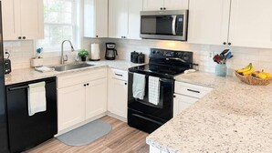 A modern kitchen with white cabinets, a black stove, a microwave, and a granite countertop. - The Gathering Place - 1 Block from Beach! (Emerald Isle)