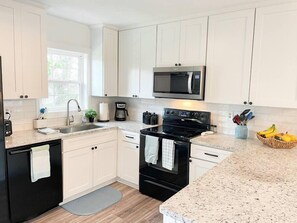 A modern kitchen with white cabinets, a black stove, a microwave, and a granite countertop. - The Gathering Place - 1 Block from Beach! (Emerald Isle)