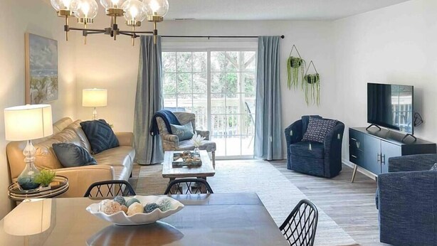 A modern living room with a sofa, armchairs, a dining table, and a TV. - The Gathering Place - 1 Block from Beach! (Emerald Isle)
