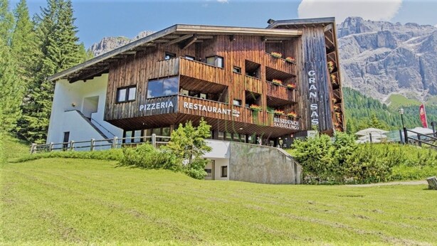 A wooden building with balconies, labeled "PIZZERIA RESTAURANT" and "GRAN SASOLUNCO RESIDENCE." - Studio apartment in front of Sassolungo mountain (Trentino-Alto Adige)