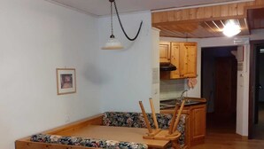 A wooden dining area with a bench and chairs, a hanging light fixture, and wooden cabinets. - Studio apartment in front of Sassolungo mountain (Trentino-Alto Adige)