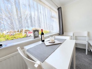 A room with a white table, a clock, a bottle of wine, and a glass of milk on the windowsill.