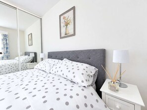 A hotel room with a bed, a nightstand, a lamp, and a mirror. - Beachfront Apt w/ Sea Views & Free Parking (Pevensey)