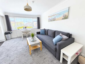 Un salon moderne avec un canapé gris, une table basse blanche et un tableau représentant une sc ène de plage.