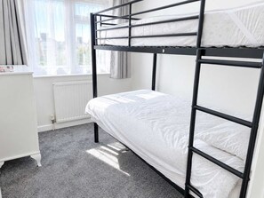 Uma cama beliche com colchão branco e janela com cortinas.