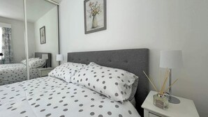 A bedroom with a bed, a nightstand, a lamp, a mirror, and a picture on the wall.