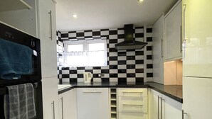 A compact kitchen with white cabinets, a black and white checkered backsplash, a window, and a built-in oven.